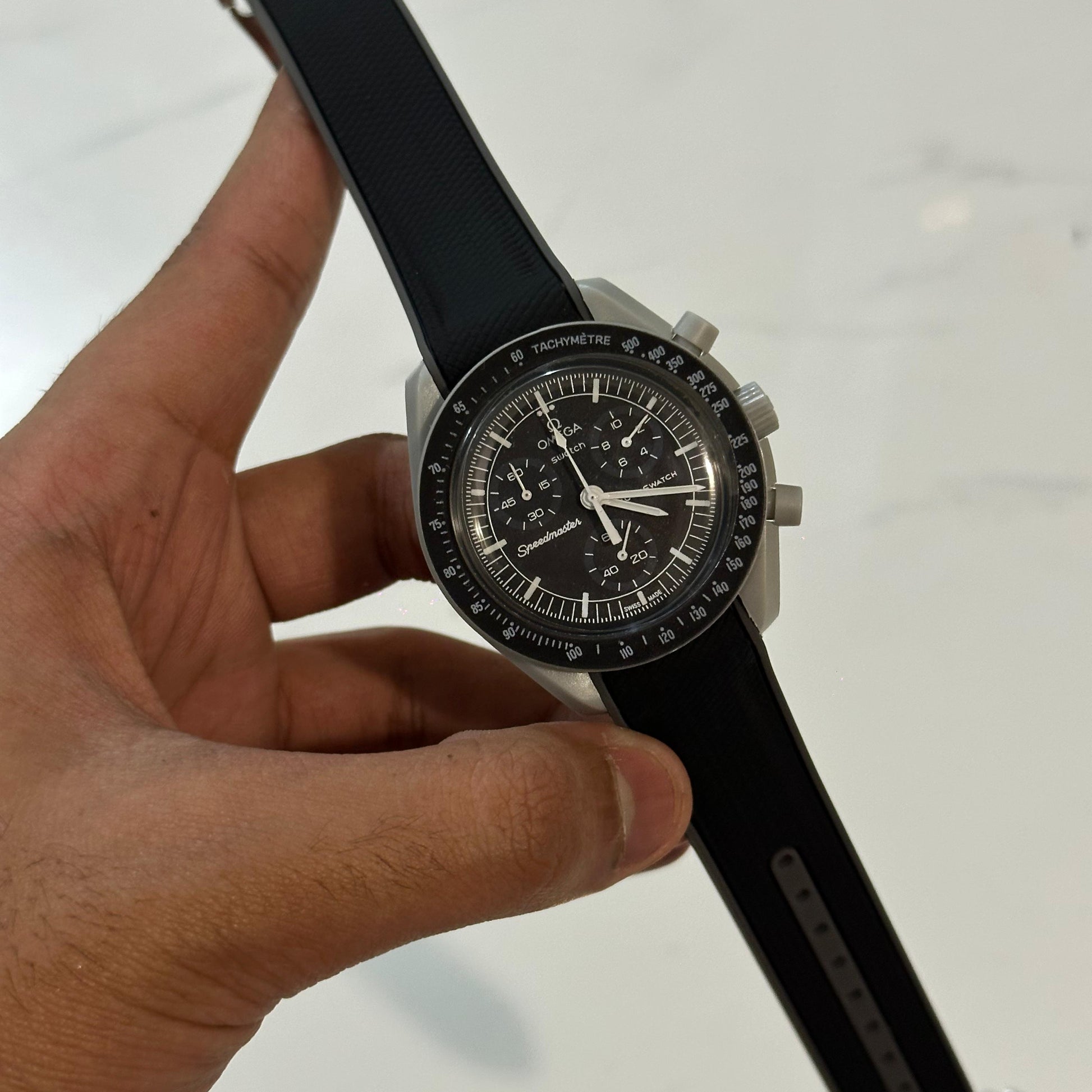 Hand holding a black wristwatch with a detailed face against a light background